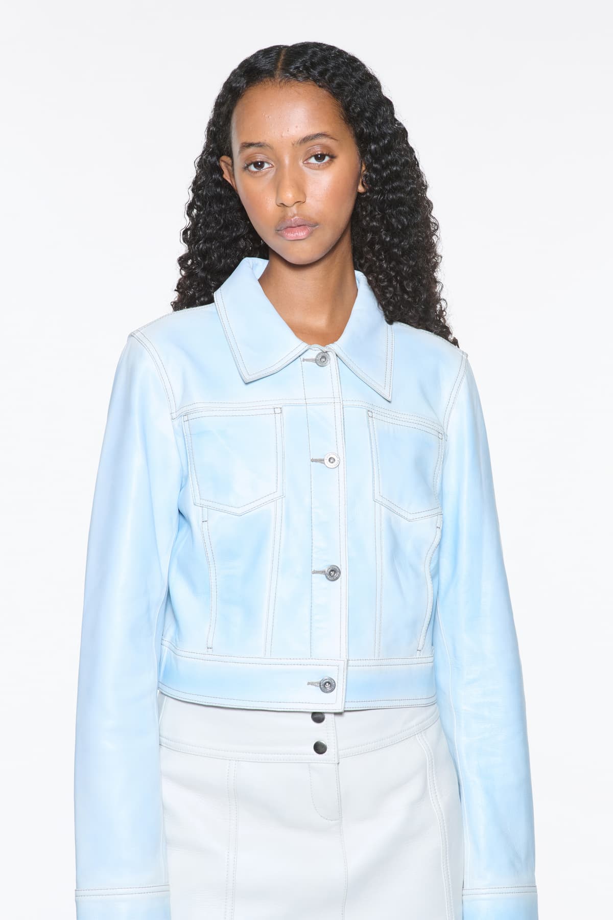 Close-up view of the Calliope Jacket in Blue Lagoon, is crafted in supple lamb leather and features a cropped silhouette. The color is a soft light blue.