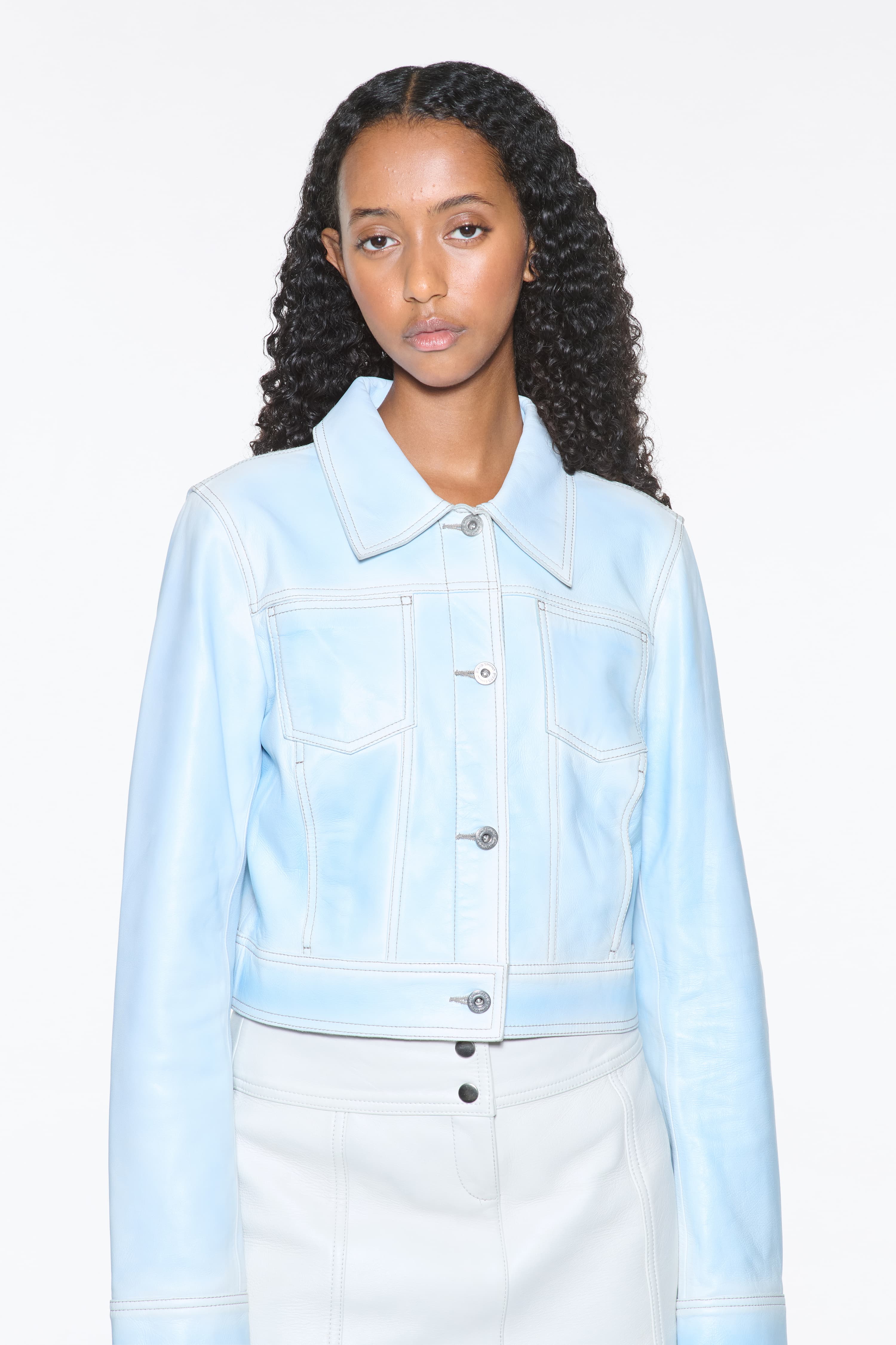 Close-up view of the Calliope Jacket in Blue Lagoon, is crafted in supple lamb leather and features a cropped silhouette. The color is a soft light blue.