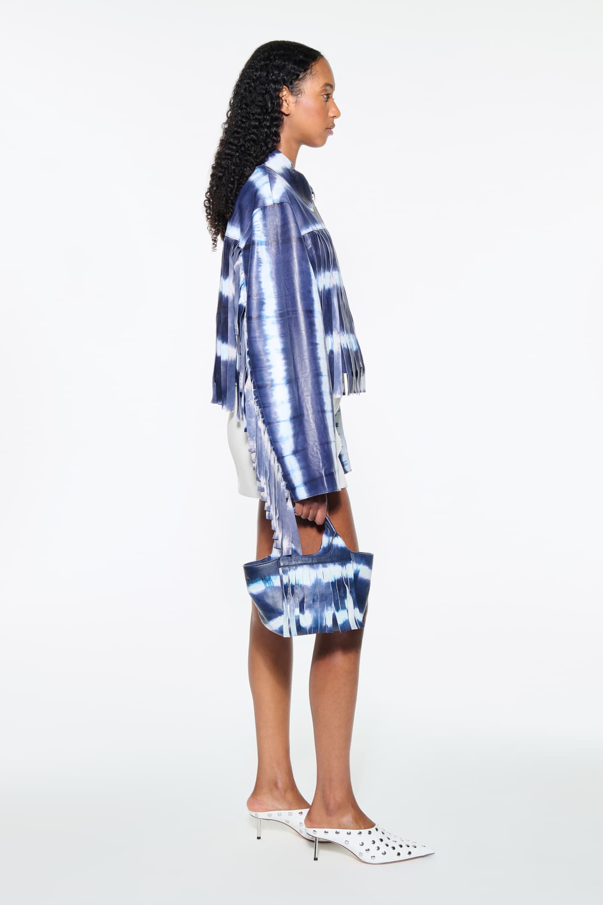 Side view of the Charlotta Fringe Jacket in Ocean Tie Dye, is designed in leather with a cropped silhouette and raw edge finishes. The color is a dark blue with white tie-dye pattern.