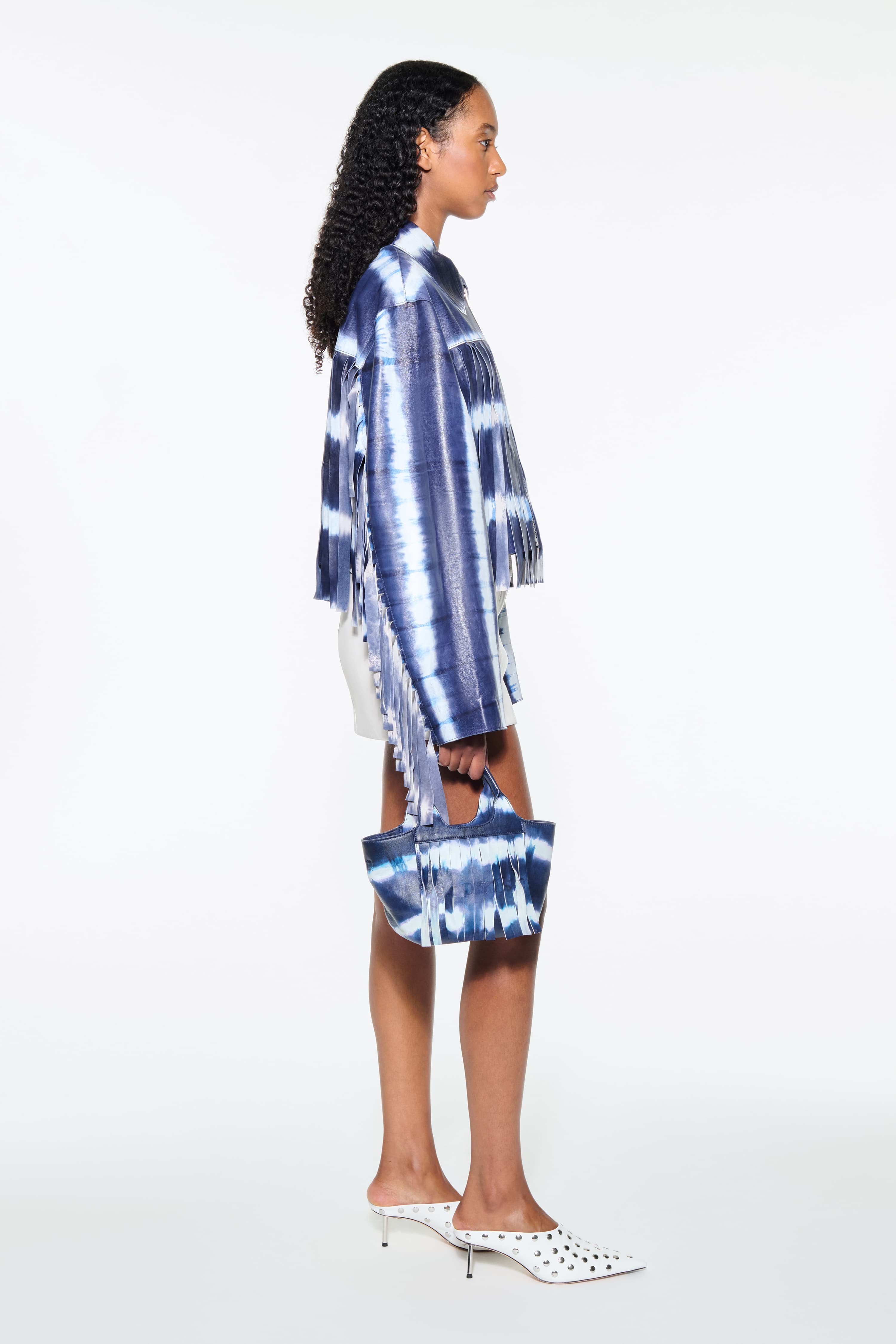 Side view of the Charlotta Fringe Jacket in Ocean Tie Dye, is designed in leather with a cropped silhouette and raw edge finishes. The color is a dark blue with white tie-dye pattern.