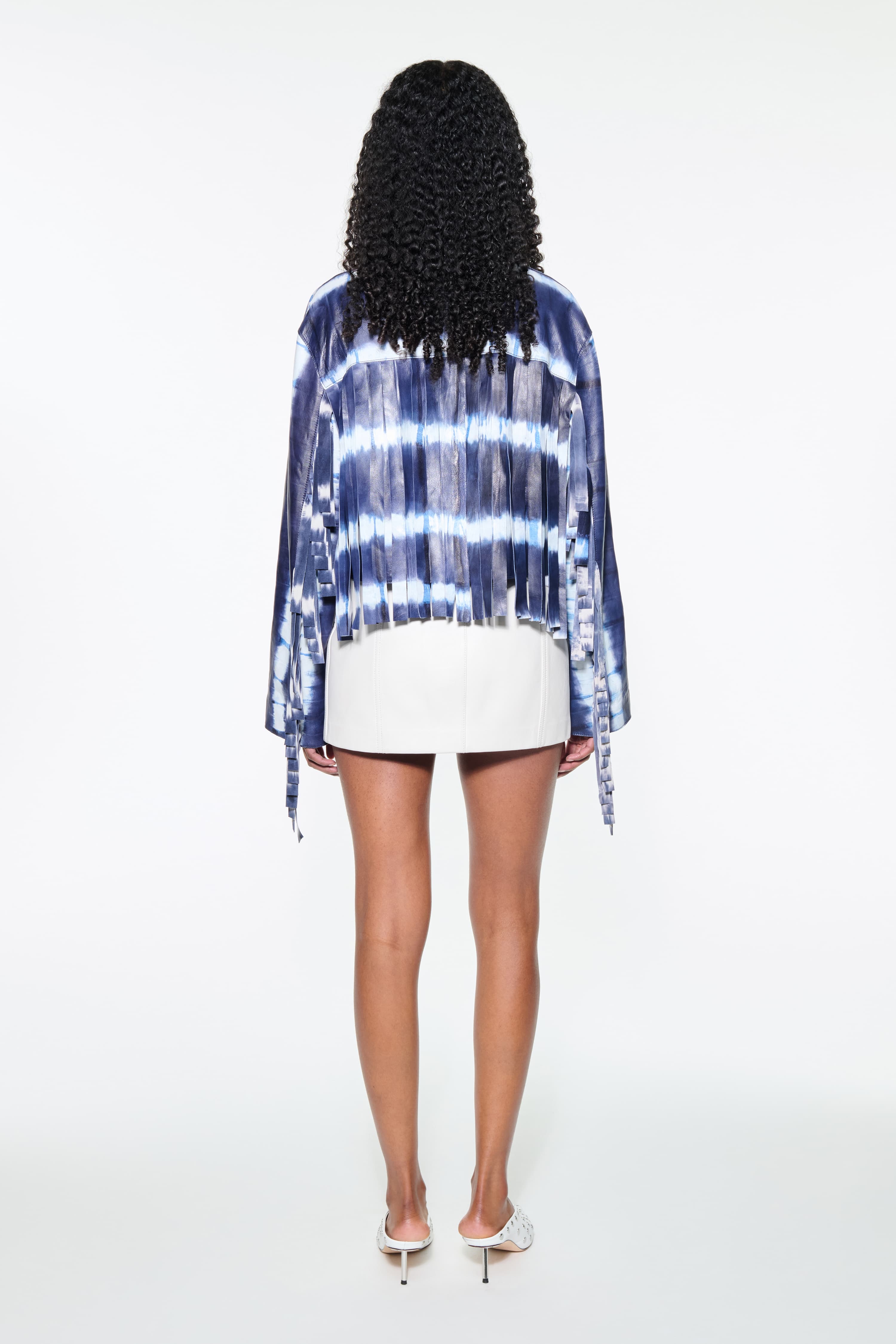 Back view of the Charlotta Fringe Jacket in Ocean Tie Dye, is designed in leather with a cropped silhouette and raw edge finishes. The color is a dark blue with white tie-dye pattern.