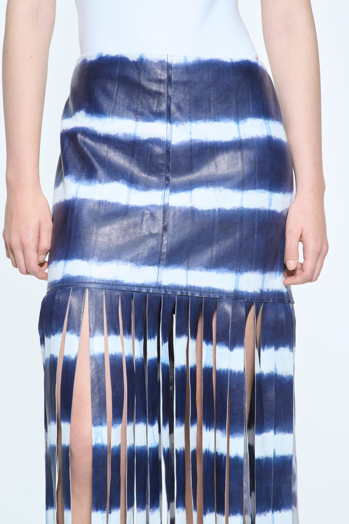 Close-up view of the Viviana Fringe Skirt in Ocean Tie Dye, is made from leather and features a clean, contemporary silhouette with raw edge fringes. The color is a dark blue with white tie-dye pattern.
