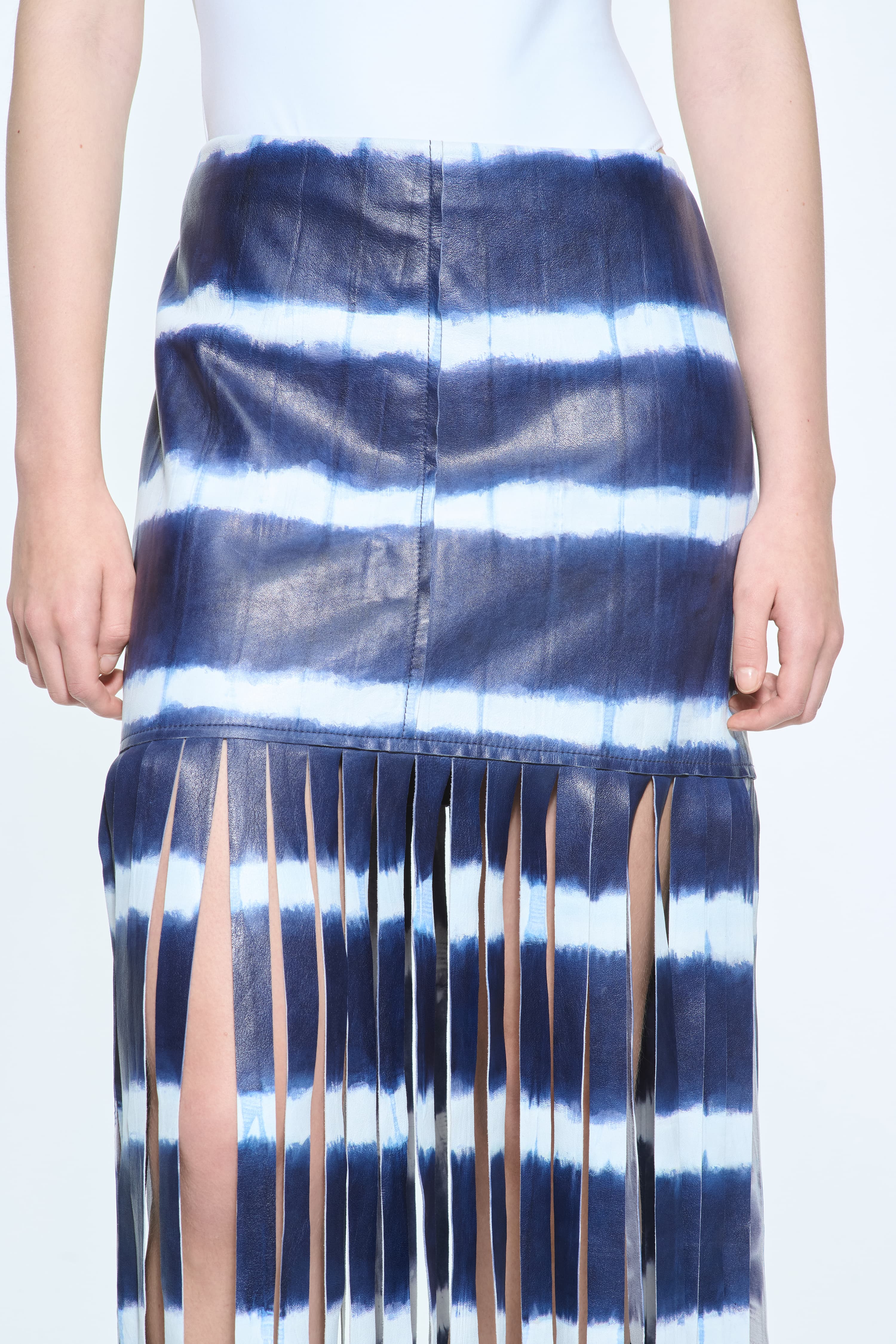 Close-up view of the Viviana Fringe Skirt in Ocean Tie Dye, is made from leather and features a clean, contemporary silhouette with raw edge fringes. The color is a dark blue with white tie-dye pattern.
