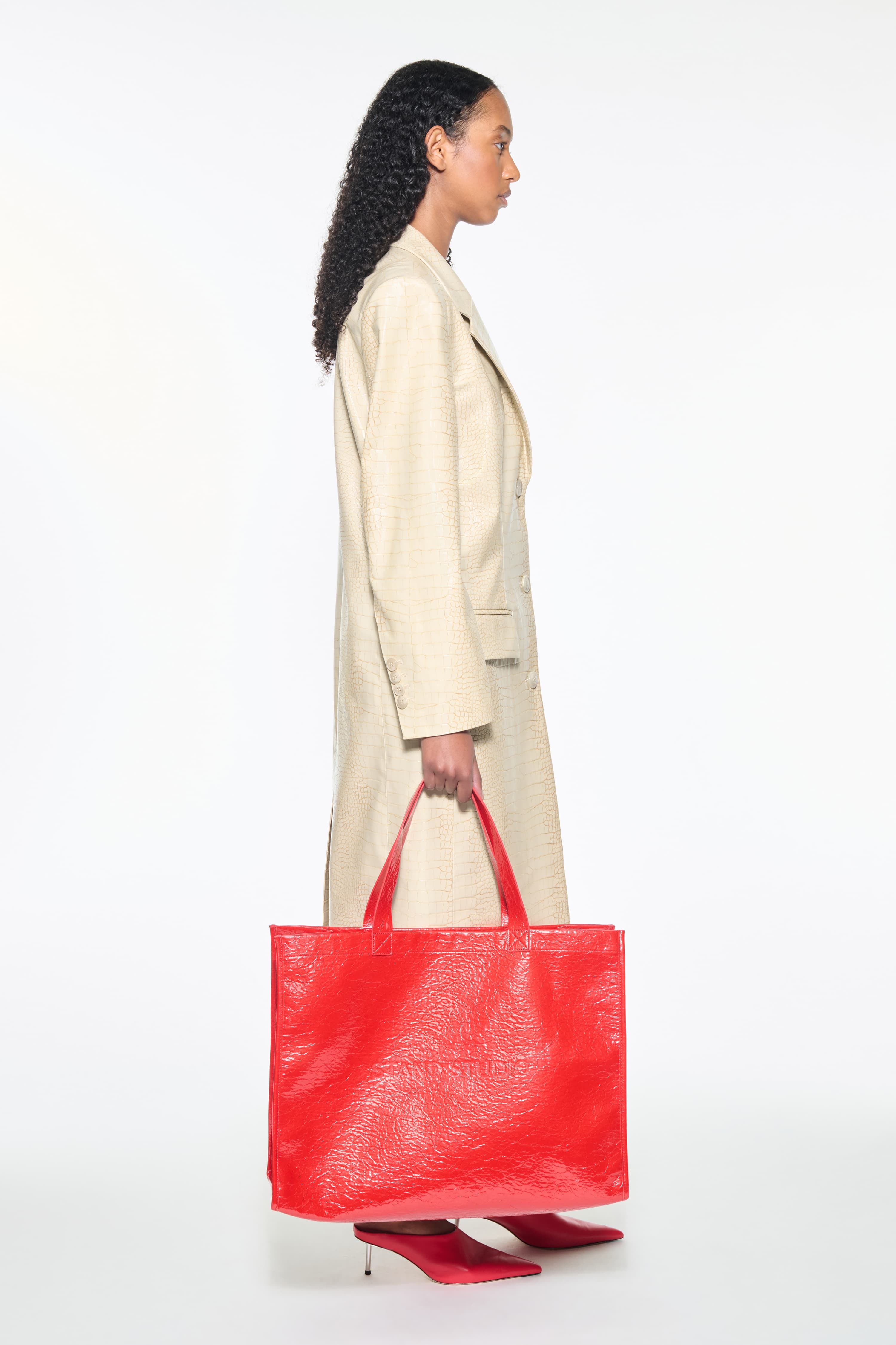 Side view of the Nicki Coat in Seashell, is a faux leather trench coat with a shiny croco pattern. The color is a creamy white tone.