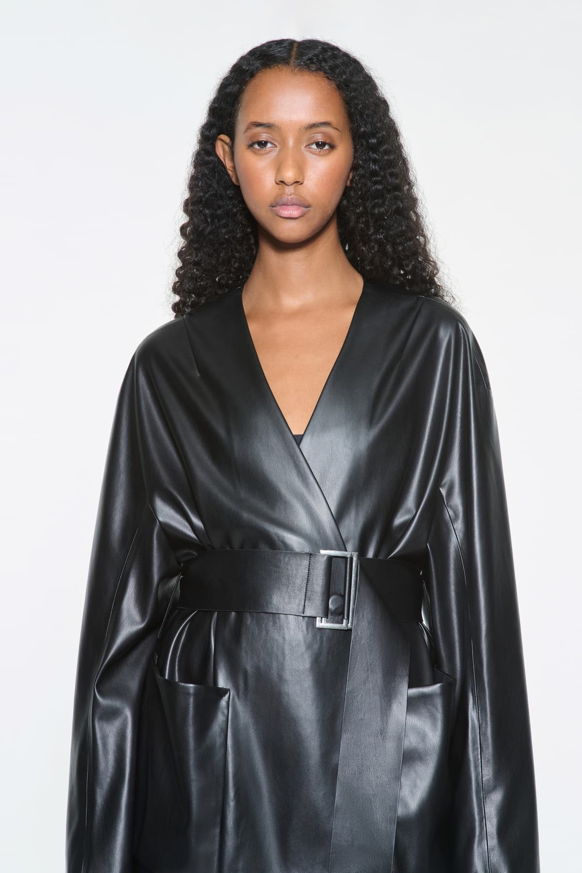 Close-up view of the Noria Jacket in Black, is a faux leather jacket with a wrap design and a belted waist.