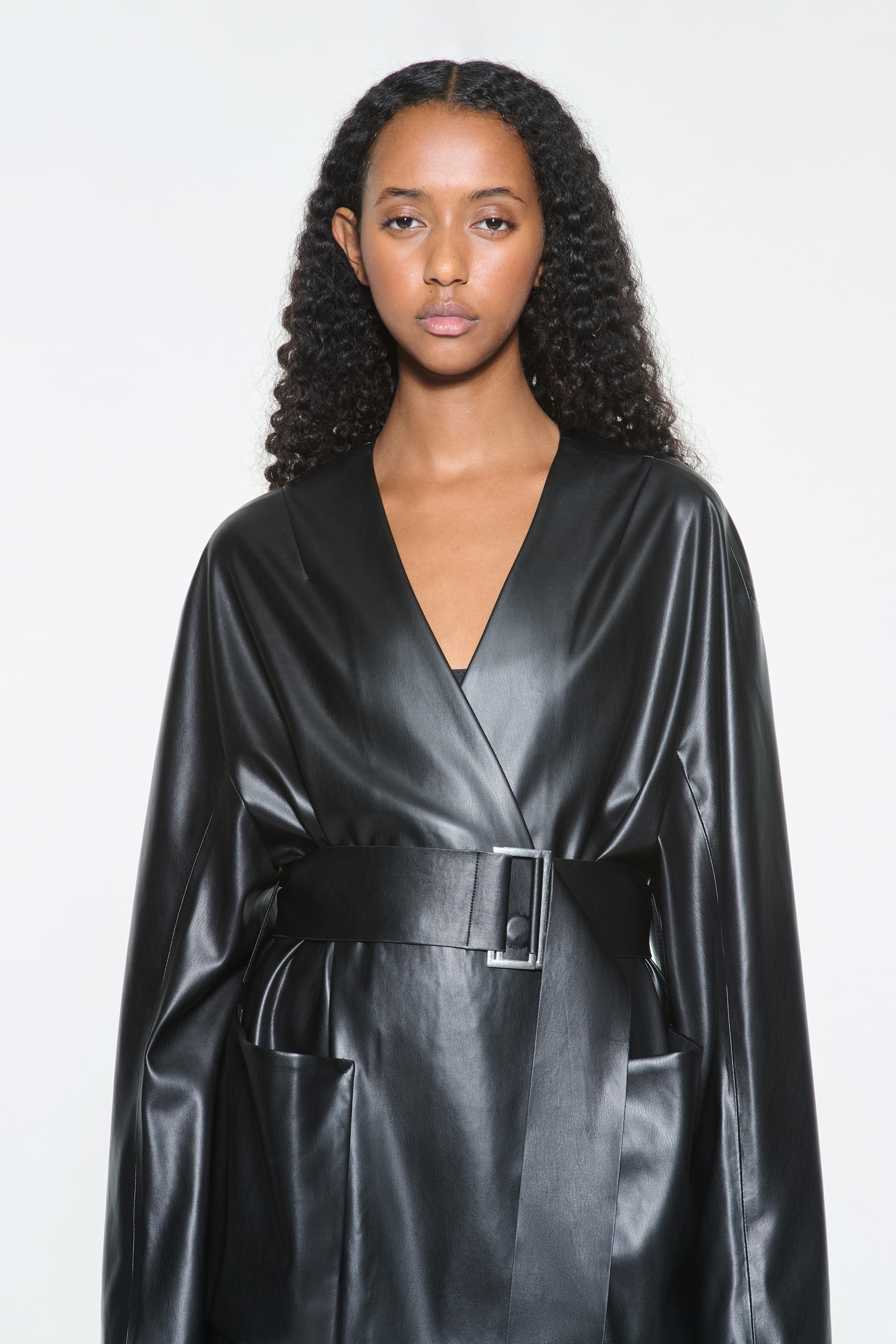 Close-up view of the Noria Jacket in Black, is a faux leather jacket with a wrap design and a belted waist.