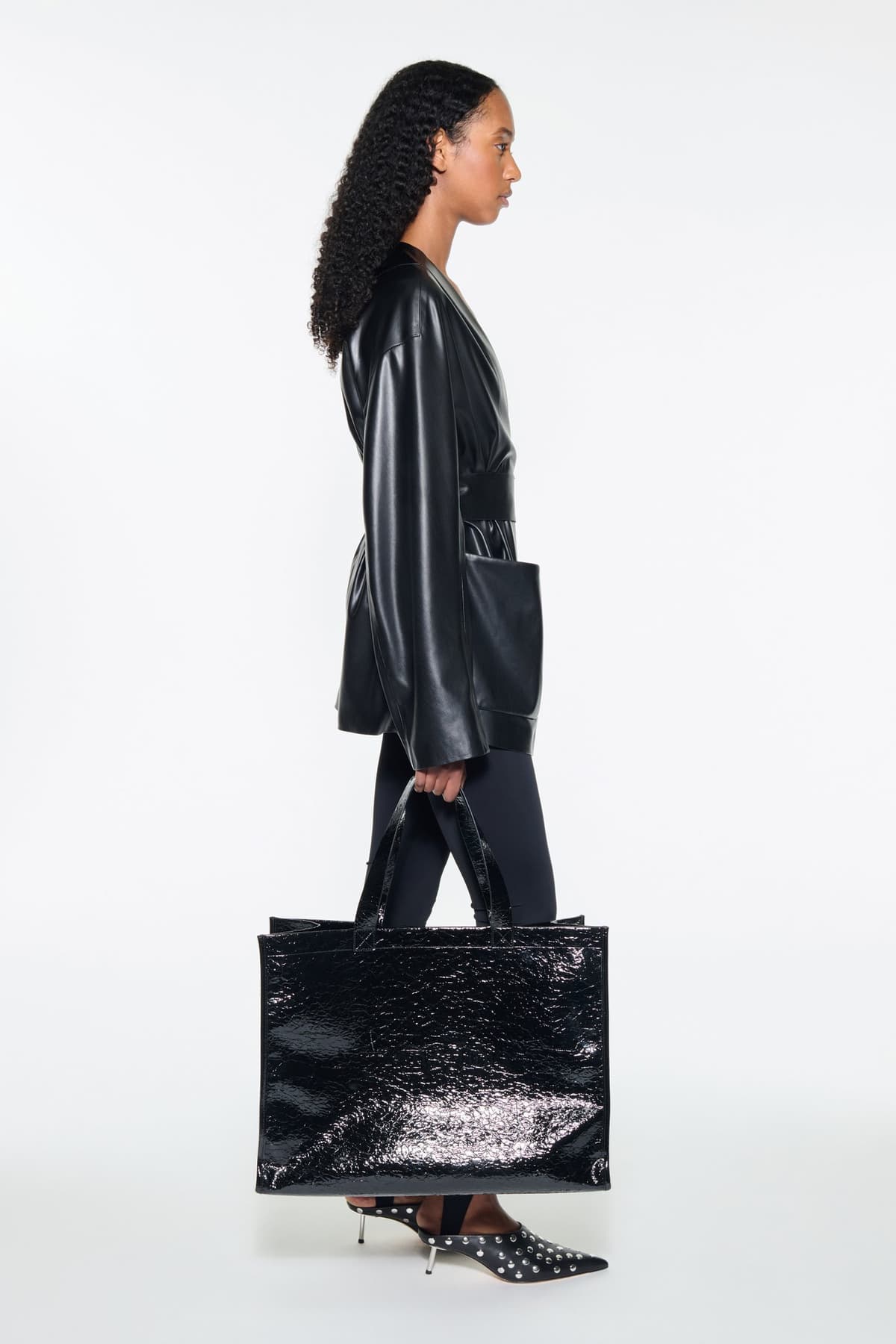 Side view of the Noria Jacket in Black, is a faux leather jacket with a wrap design and a belted waist.