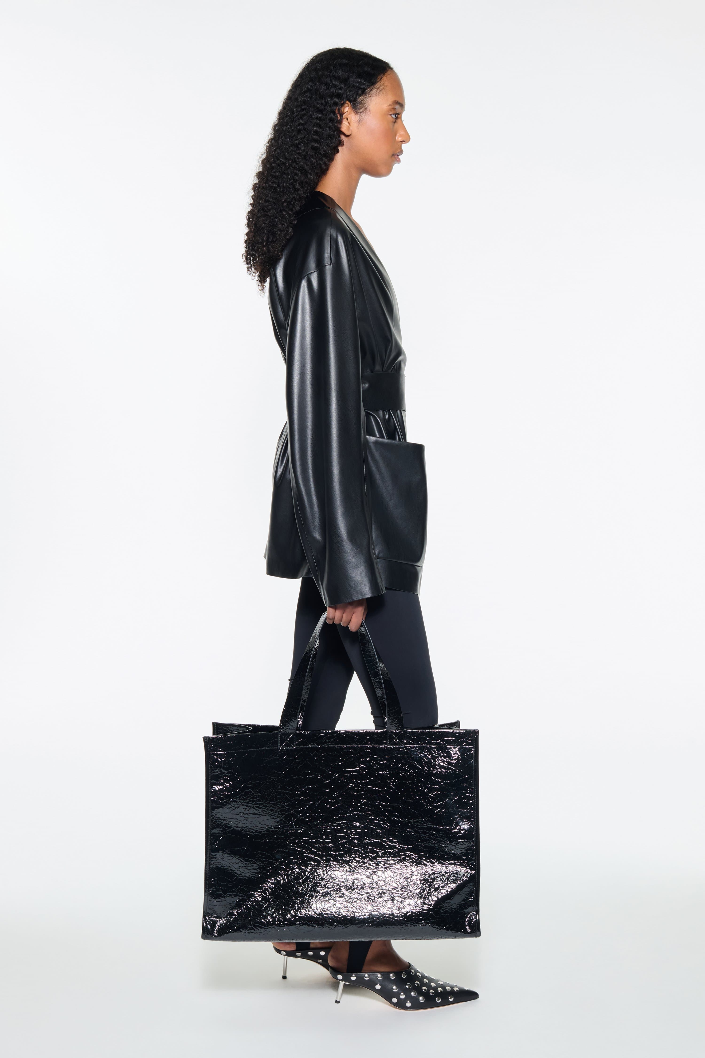 Side view of the Noria Jacket in Black, is a faux leather jacket with a wrap design and a belted waist.