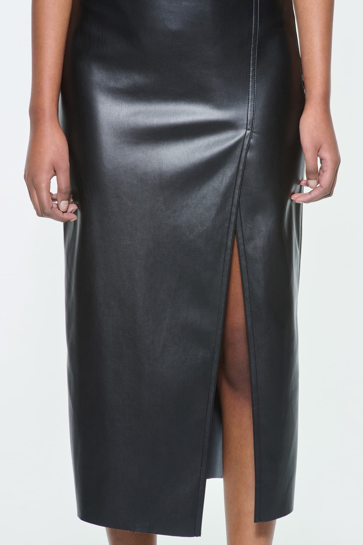 Close-up view of the Kamila Skirt in Black, is a faux leather midi skirt with a high slit at the front.