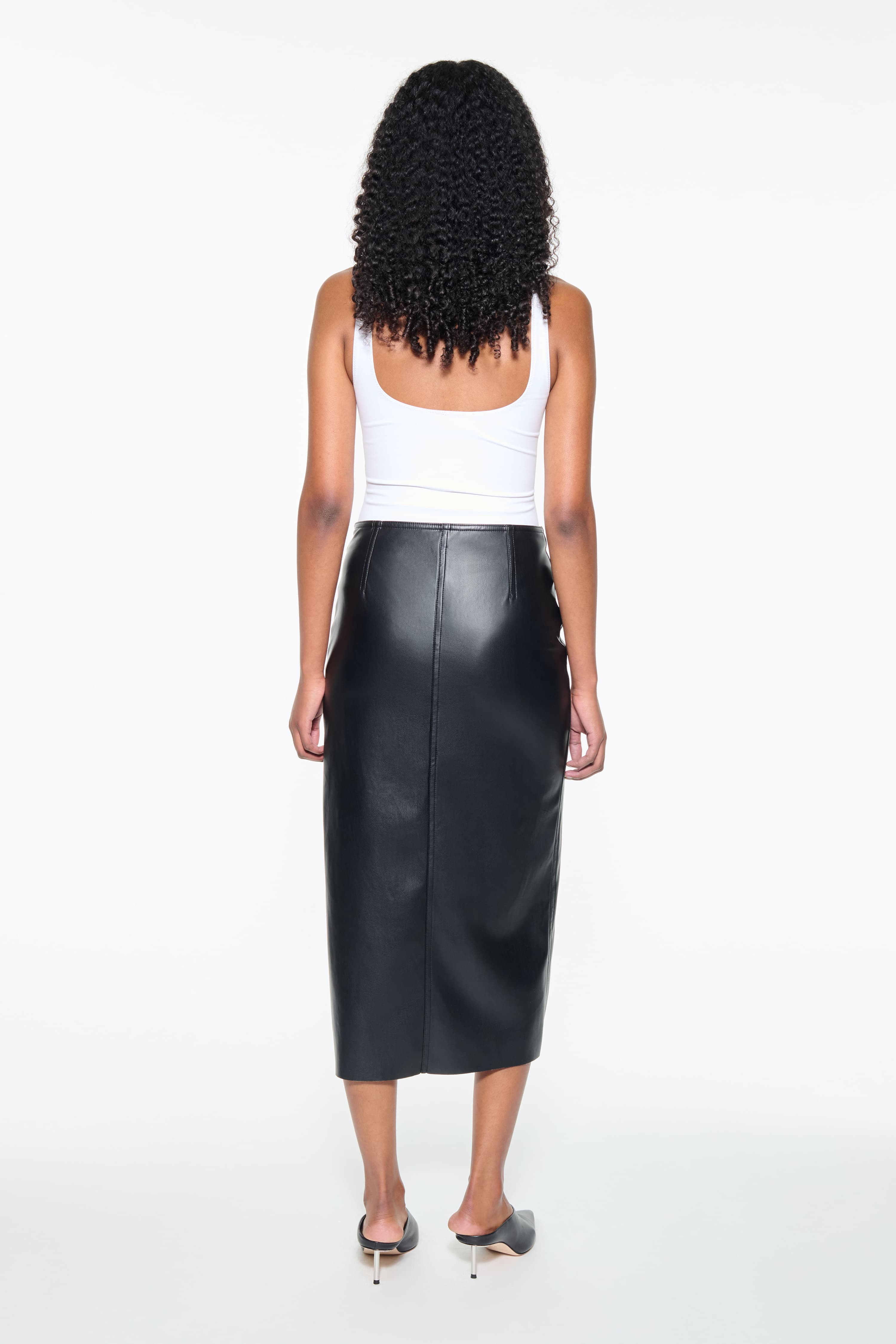 Back view of the Kamila Skirt in Black, is a faux leather midi skirt with a high slit at the front.