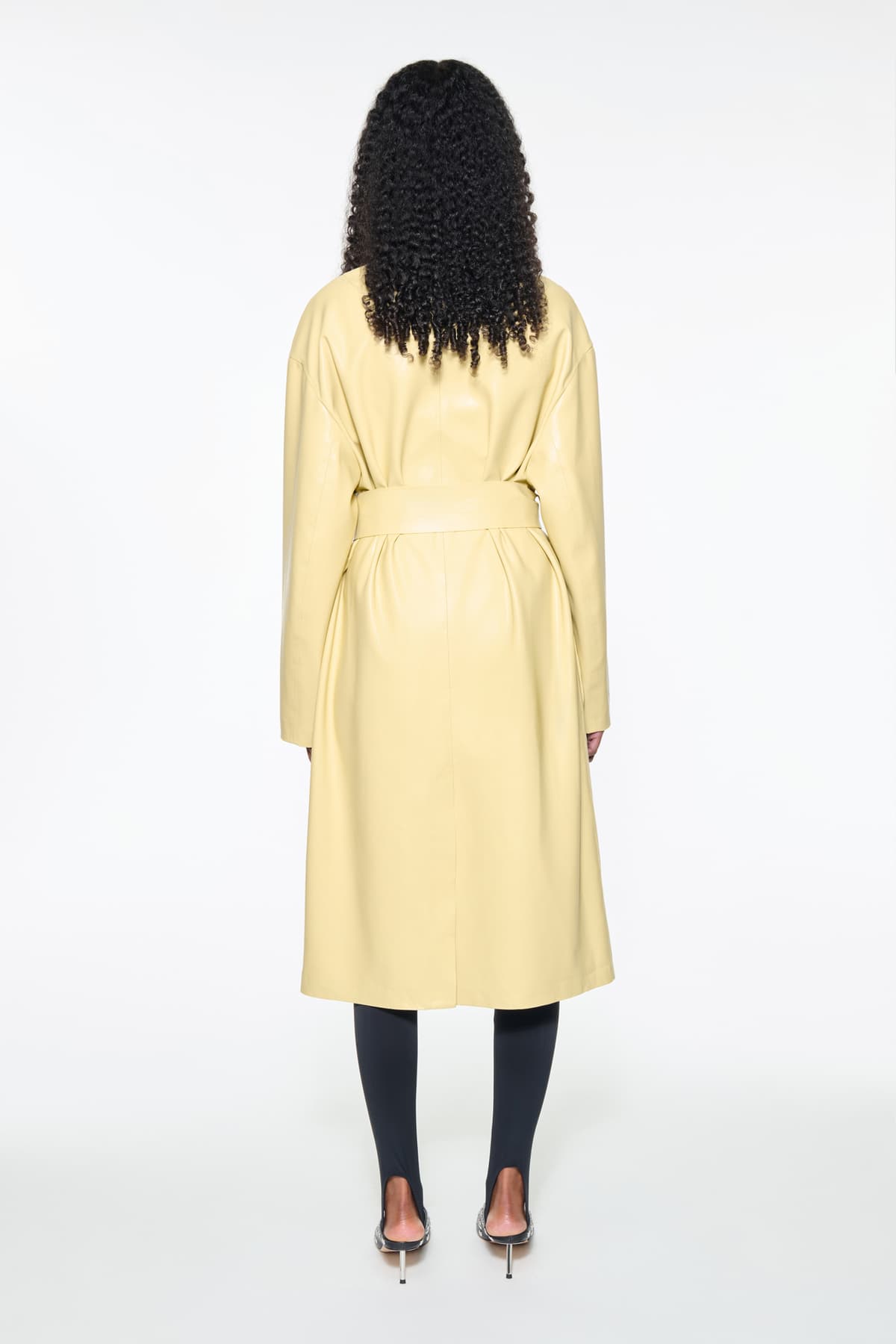 Back view of the Valeria Coat in Pina Colada, is a faux leather coat with a wrap design and a belted waist. The color is a pale yellow tone.