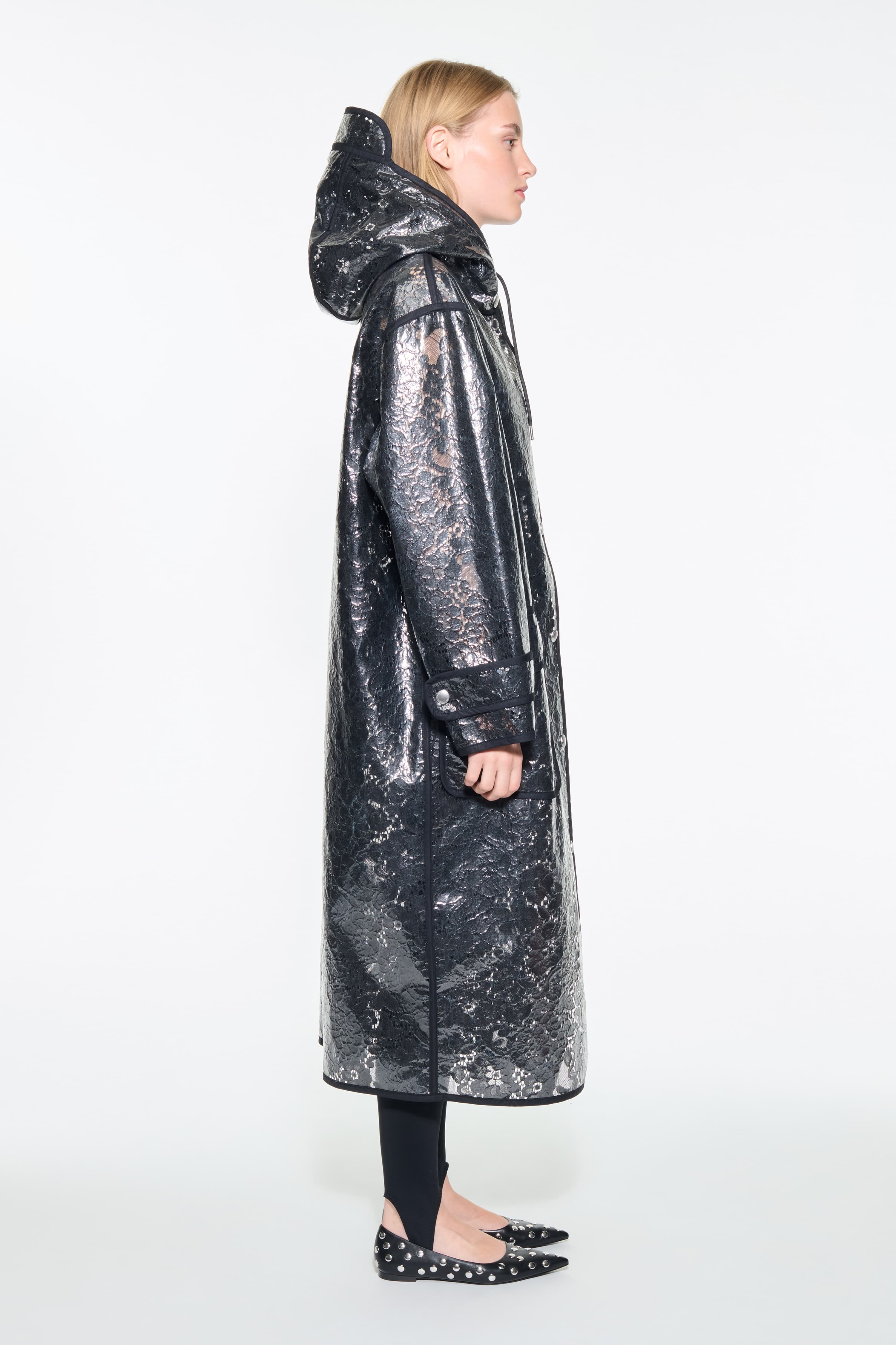 Side view of the True Raincoat in Black, is a lightweight raincoat with a lace-patterned design.