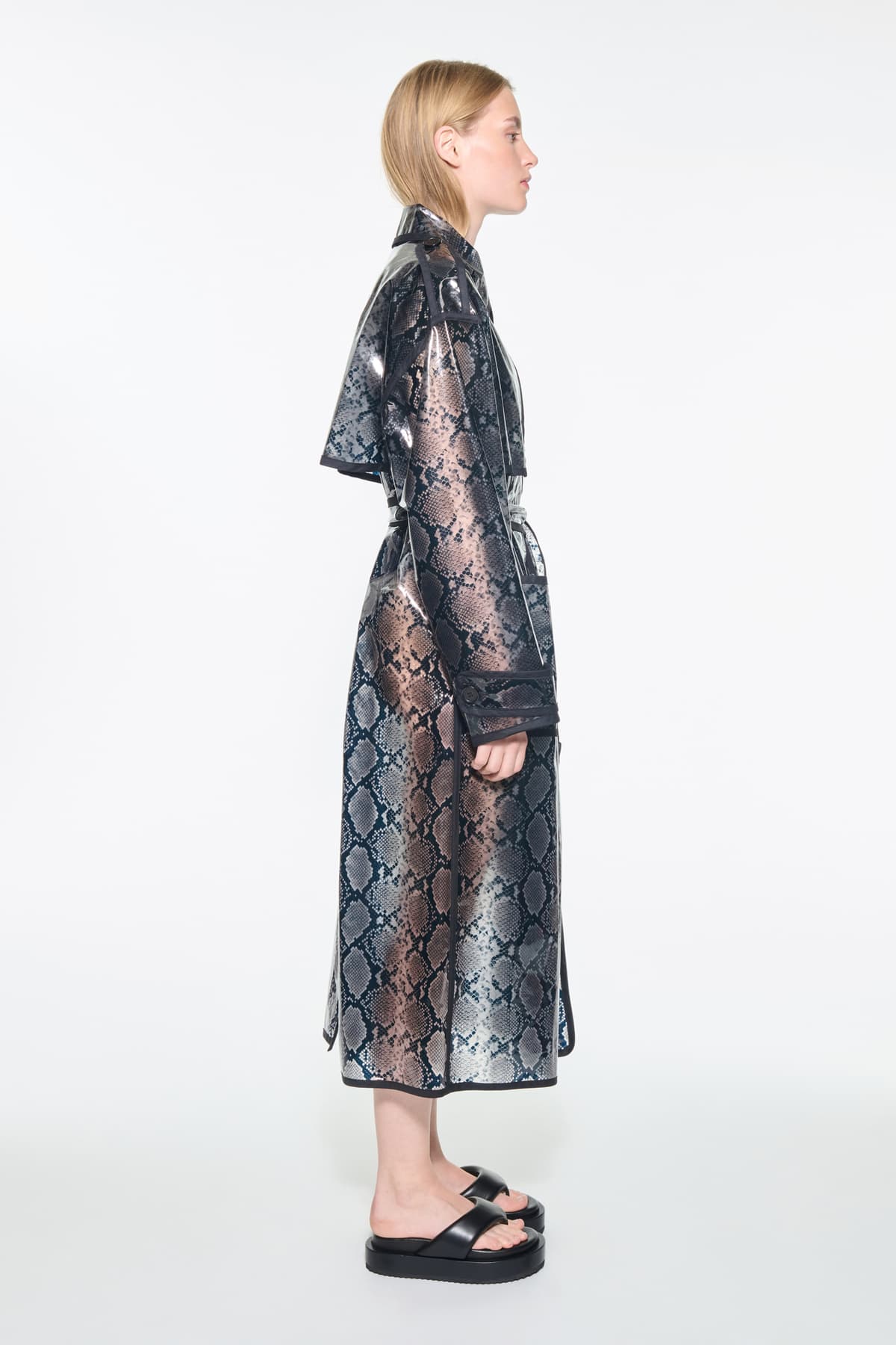 Side view of the Promise Raincoat in Black, is a lightweight raincoat with a glossy snake-patterned finish.